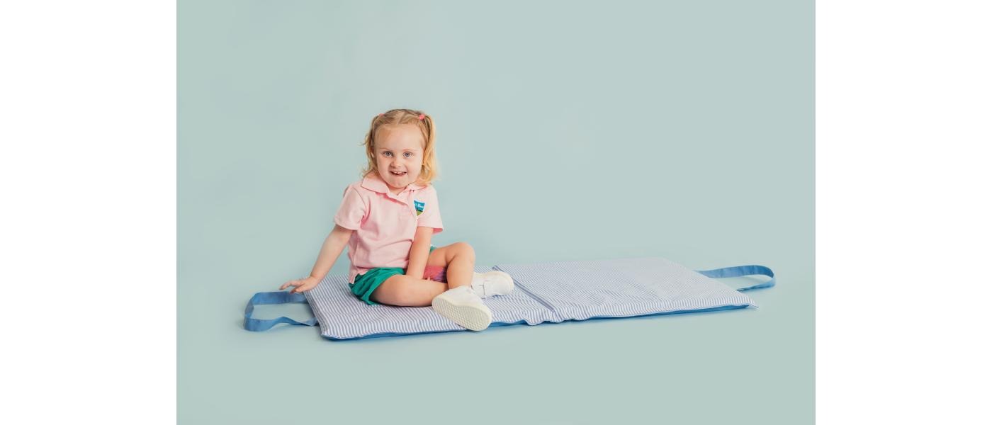 Niña sentada sobre márfega colchoneta escolar
